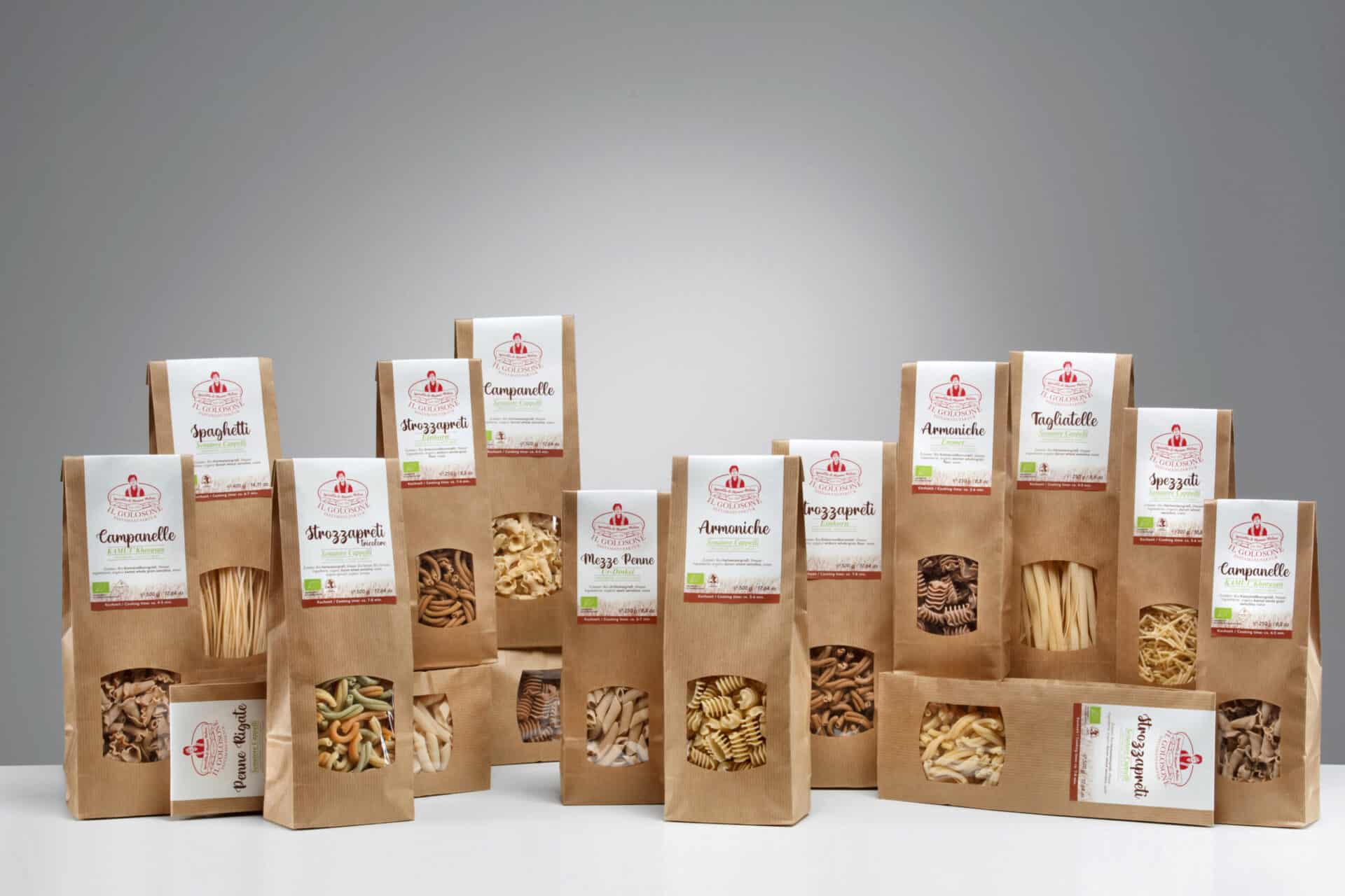Verschiedene italienische Pasta Marken in braunen Verpackungen, einzeln verpackt, auf weißem Tisch, hinter grauem Hintergrund.